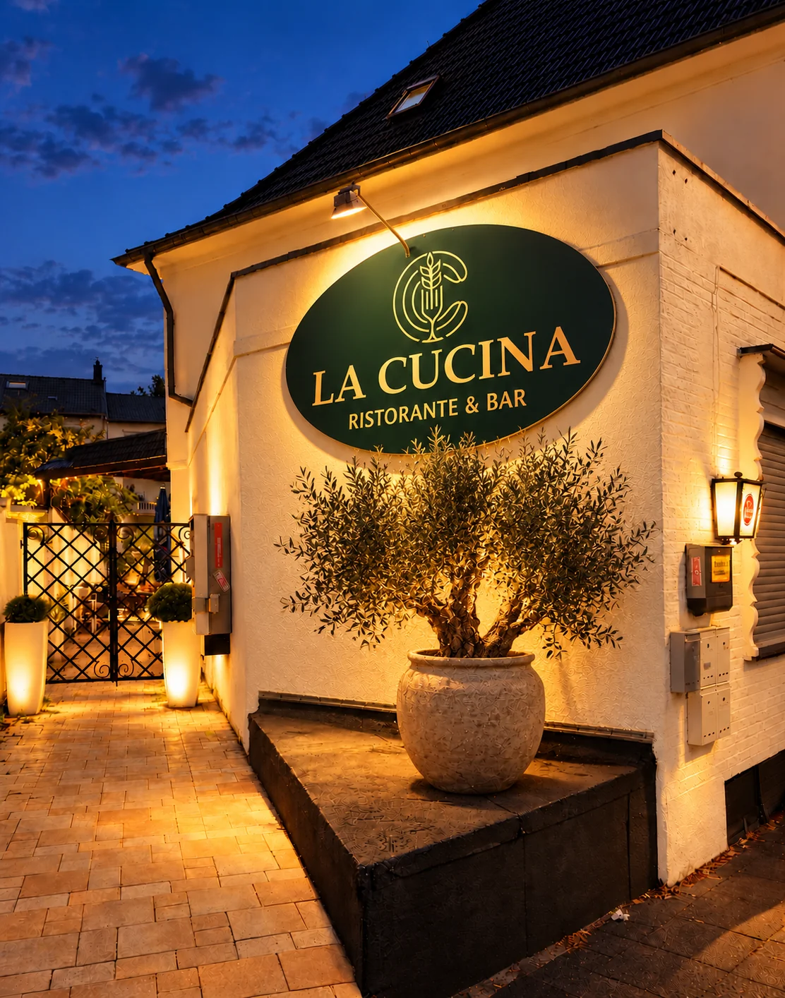 Hausecke mit dem grünen La-Cucina-Schild am Abend